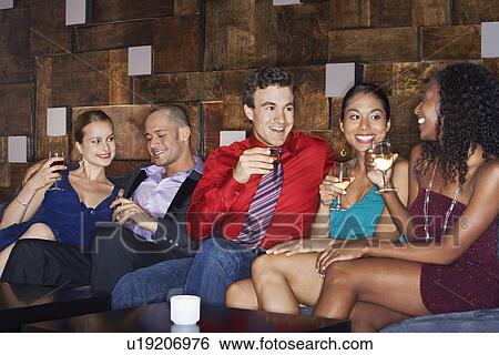 Stock Photograph - Friends talking and drinking while sitting in bar. Fotosearch