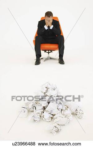 Stock Photo - Frustrated businessman sitting near pile of crumpled paper. Fotosearch