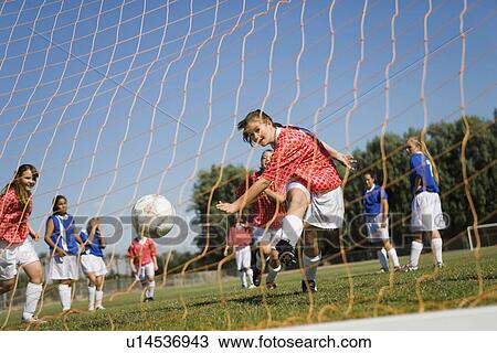Stock Image - Girl (13-17) scoring with soccer ball. Fotosearch