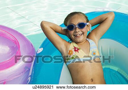 Stock Image - Girl (7-9) lying on inflatable raft in swimming pool view from above portrait.. Fotosearch