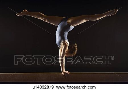 Stock Photo - Gymnast (13-15) doing split handstand on balance beam side view. Fotosearch