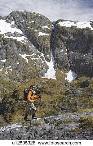 Stock Photograph - Hiker climbing trail in steep mountains. Fotosearch
