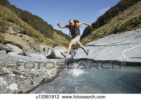 Stock Image - Hiker jumping across river. Fotosearch