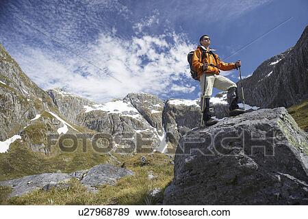 Stock Photo - Hiker on top of boulder in mountains. Fotosearch