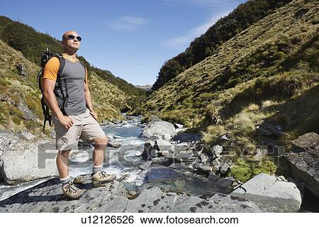Hiker standing by edge of river View Large Photo Image Stock Photograph - Hiker standing by edge of river. Fotosearch
