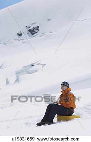Stock Photo - Hiker using laptop on snowy mountain peak. Fotosearch