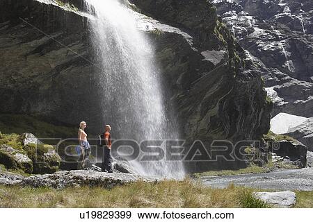 Hikers standing under waterfall at river View Large Photo Image Stock Photo - Hikers standing under waterfall at river. Fotosearch