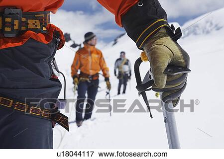 Stock Photo - Hikers using walking sticks in snowy mountains mid section on front man. Fotosearch