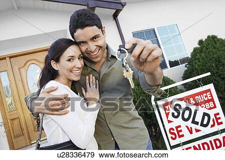 Homeowners standing in front of house with Sold sign holding key portrait View Large Photo Image Stock Photo - Homeowners standing in front of house with Sold sign holding key portrait. Fotosearch