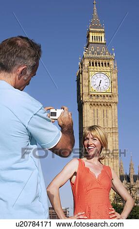 Stock Image - Husband taking photo of wife by Big Ben Tower London England. Fotosearch