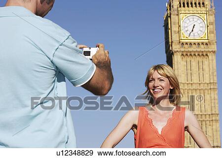 Stock Photo - Husband taking photo of wife by Big Ben Tower London England. Fotosearch