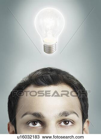 Stock Image - Illuminated lightbulb over man's head high section studio shot. Fotosearch