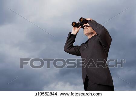 Low angle view of businessman looking through binoculars against stormy sky View Large Photo Image Picture - Low angle view of businessman looking through binoculars against stormy sky. Fotosearch