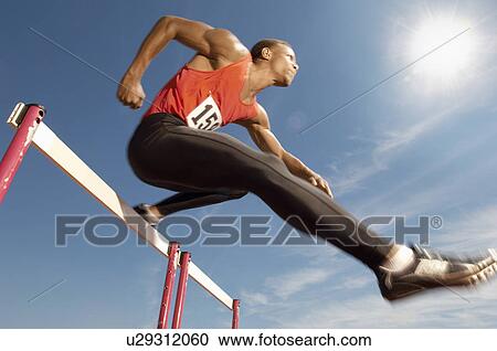 Male athlete jumping hurdle mid air View Large Photo Image Stock Image - Male athlete jumping hurdle mid air. Fotosearch