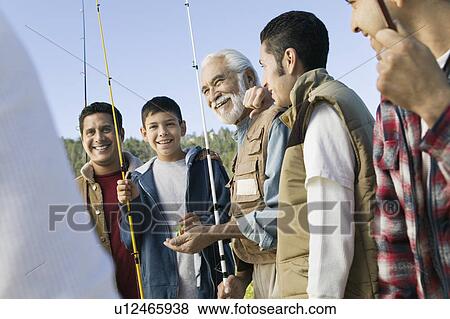 Stock Photo - Male members of three generation family holding fishing rods outdoors smiling. Fotosearch