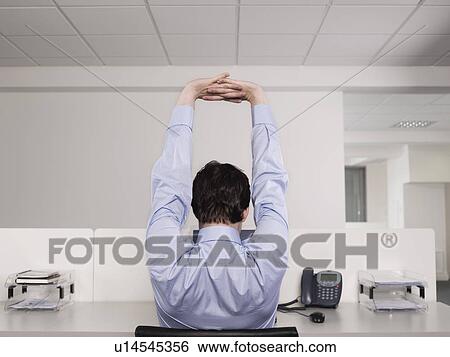 Male office worker stretching at desk View Large Photo Image Stock Photograph - Male office worker stretching at desk. Fotosearch