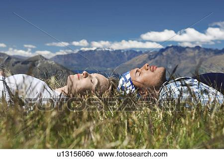 Stock Image - Man and woman lying in field overlooking hills. Fotosearch