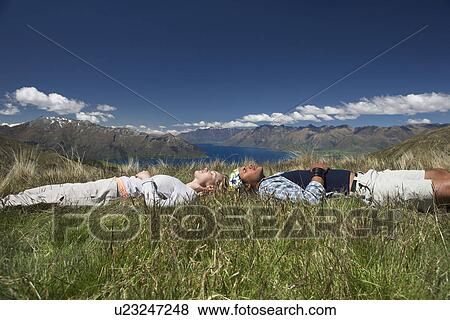 Stock Photo - Man and woman lying in field overlooking hills and lakes. Fotosearch