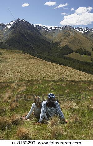Man and woman sitting in grass looking at mountains back view View Large Photo Image Stock Photo - Man and woman sitting in grass looking at mountains back view. Fotosearch