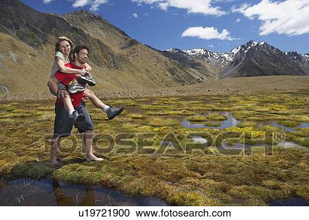 Man giving woman piggy-back ride through pond near mountains View Large Photo Image Stock Image - Man giving woman piggy-back ride through pond near mountains. Fotosearch