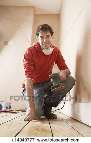 Stock Photo - Man holding sanding tool in unrenovated room portrait. Fotosearch
