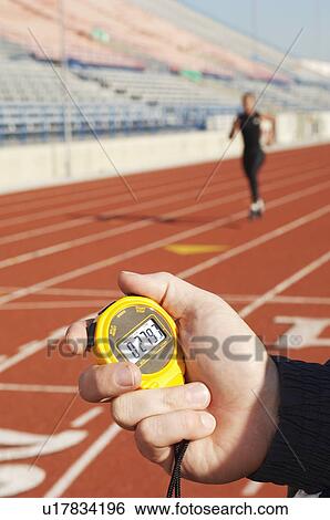 Stock Photograph - Man holding stopwatch close up of hand timing runner on running track. Fotosearch