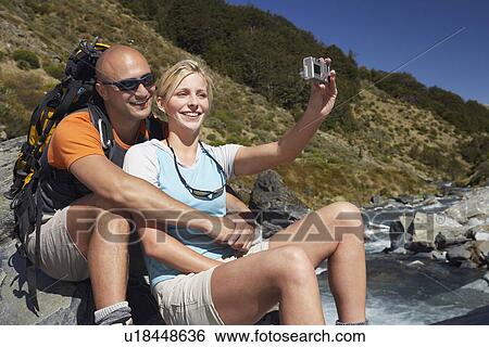 Man hugging woman as she takes their picture by a river in a forest View Large Photo Image Stock Photograph - Man hugging woman as she takes their picture by a river in a forest. Fotosearch