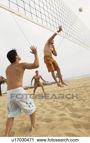 Stock Image - Man in Mid-air Going for Volleyball on beach. Fotosearch