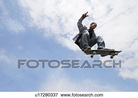 Stock Photo - Man jumping on skateboard in air low angle view. Fotosearch