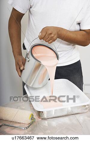 Stock Photo - Man pouring paint into tray mid section. Fotosearch