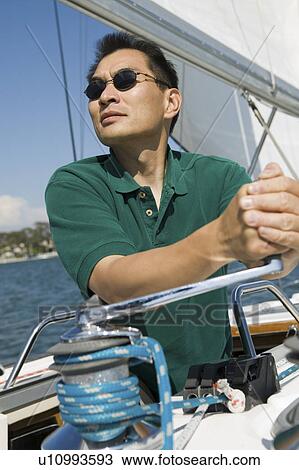 Stock Image - Man raising sail on sailboat. Fotosearch