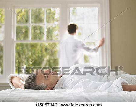 Man relaxing in bed wife looking through window in background View Large Photo Image Stock Photo - Man relaxing in bed wife looking through window in background. Fotosearch