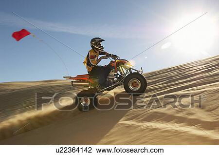 Stock Image - Man riding quad bike in desert. Fotosearch