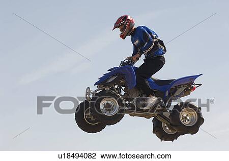 Man riding quad bike in mid-air against blue sky close up View Large Photo Image Stock Image - Man riding quad bike in mid-air against blue sky close up. Fotosearch