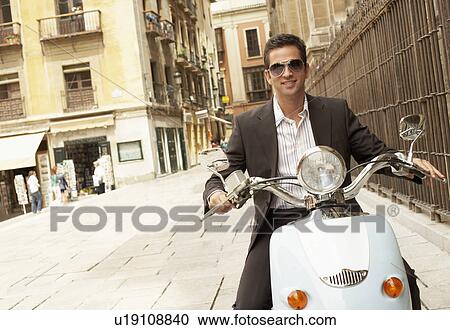 Stock Image - Man riding scooter through old town portrait.. Fotosearch