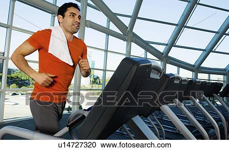 Stock Image - Man running on treadmill in gymnasium. Fotosearch