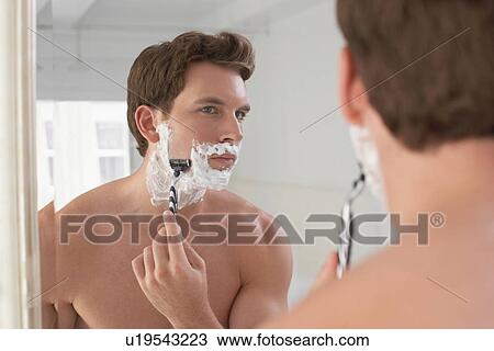 Stock Image - Man shaving in bathroom mirror. Fotosearch
