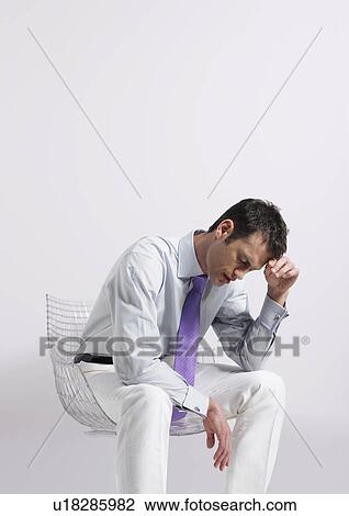 Stock Image - Man sitting in chair with head in hand in studio. Fotosearch
