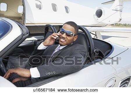 Man sitting in Convertible near private jet talking on mobile View Large Photo Image Picture - Man sitting in Convertible near private jet talking on mobile. Fotosearch