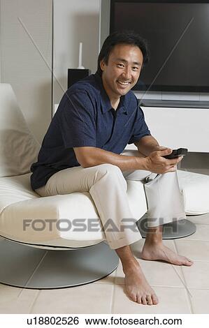 Man Sitting in Modern Living Room Holding Remote portrait View Large Photo Image Stock Photograph - Man Sitting in Modern Living Room Holding Remote portrait. Fotosearch