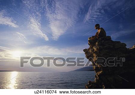 Picture - Man sitting on rock overlooking ocean. Fotosearch