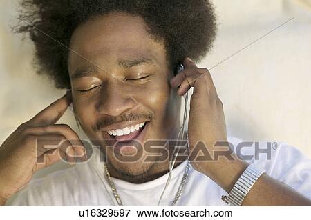 Stock Photo - Man sitting on sofa listening to music on MP3 player close up. Fotosearch
