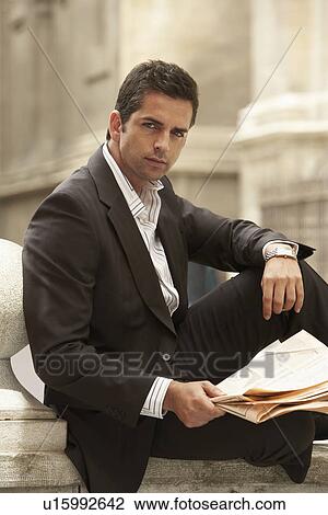 Stock Image - Man sitting outdoors holding newspaper portrait.. Fotosearch