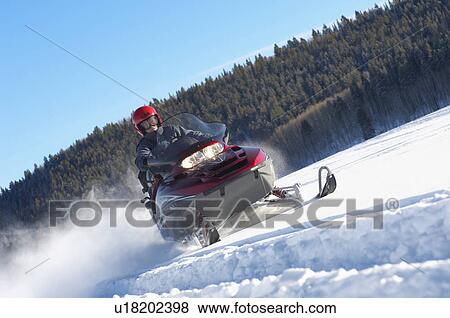 Man Snowmobiling through snow in front of forest low angle view. View Large Photo Image Stock Photo - Man Snowmobiling through snow in front of forest low angle view.. Fotosearch