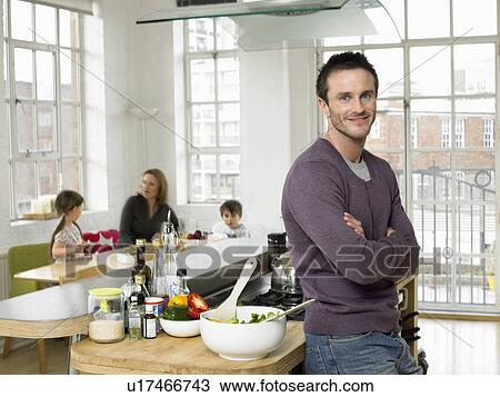 Stock Image - Man standing in kitchen smiling (portrait). Fotosearch