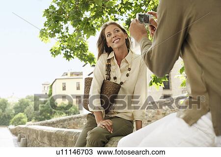 Stock Image - Man taking picture of partner on wall in Granada Spain back view low angle view. Fotosearch