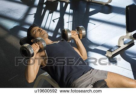 Stock Image - Man using dumbbells in gymnasium. Fotosearch