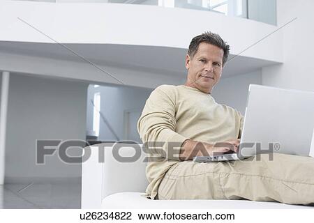 Man using laptop on sofa in living room portrait View Large Photo Image Stock Image - Man using laptop on sofa in living room portrait. Fotosearch