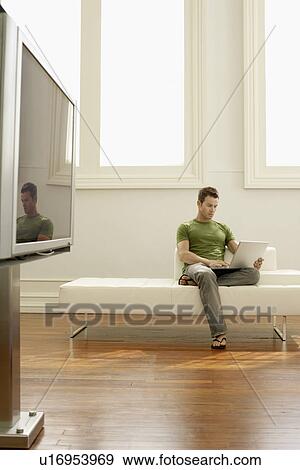 Stock Photo - Man using laptop on sofa in modern apartment. Fotosearch