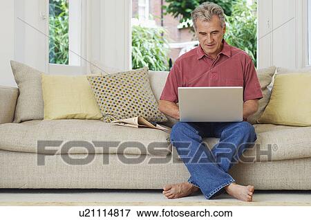 Man using laptop sat on sofa View Large Photo Image Stock Photo - Man using laptop sat on sofa. Fotosearch